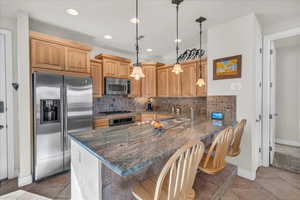 Kitchen with kitchen peninsula, a kitchen bar, stainless steel appliances, decorative light fixtures, and dark stone countertops