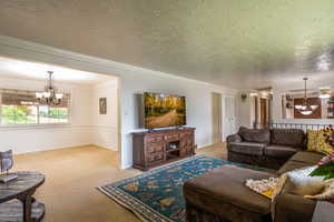 Living room with carpet flooring, a notable chandelier, crown molding, and a textured ceiling