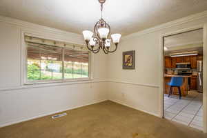 Empty room with light colored carpet, ornamental molding, and a chandelier