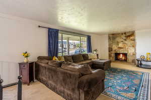 Living room with a stone fireplace, light carpet, crown molding, and a textured ceiling