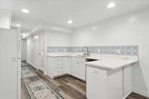 Kitchen with white cabinets, dark hardwood / wood-style flooring, kitchen peninsula, and sink