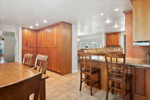 Kitchen featuring light stone countertops, kitchen peninsula, decorative backsplash, a breakfast bar, and light tile patterned floors