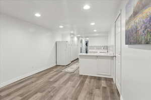 Kitchen with white cabinets, white refrigerator, sink, light wood-type flooring, and kitchen peninsula