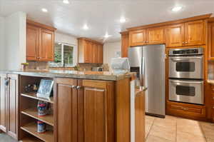 Kitchen with stainless steel appliances, light stone counters, kitchen peninsula, decorative backsplash, and light tile patterned flooring