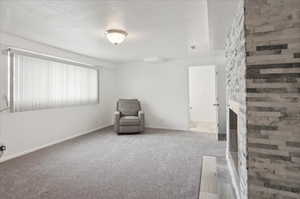 Unfurnished room featuring a stone fireplace, carpet floors, and a textured ceiling