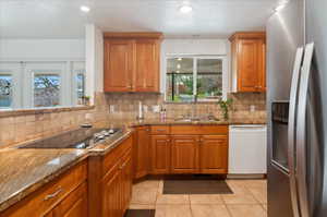 Kitchen with stainless steel refrigerator with ice dispenser, light stone counters, sink, light tile patterned floors, and dishwasher