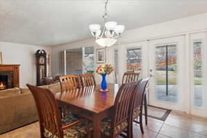 Dining room featuring a fireplace, french doors, a textured ceiling, and an inviting chandelier