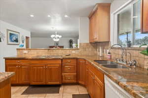 Kitchen with sink, dishwasher, a notable chandelier, dark stone countertops, and decorative backsplash