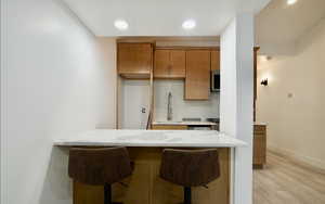 Kitchen with decorative backsplash, sink, a kitchen breakfast bar, kitchen peninsula, and light wood-type flooring