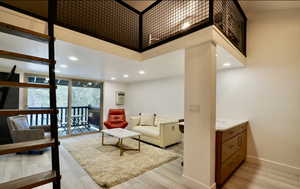 Living room with a wall unit AC, floor to ceiling windows, light hardwood / wood-style flooring, and a high ceiling