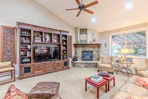 Living room featuring high vaulted ceiling, light colored carpet, a stone fireplace, and ceiling fan