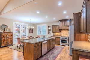 Kitchen with an inviting chandelier, sink, decorative backsplash, an island with sink, and stainless steel appliances