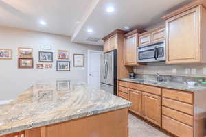 Kitchen with light stone countertops, appliances with stainless steel finishes, and sink