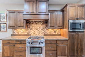 Kitchen with light stone countertops, custom range hood, stainless steel appliances, and tasteful backsplash