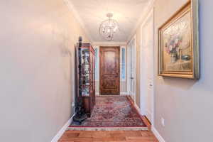 Hallway featuring crown molding, hardwood / wood-style floors, and an inviting chandelier