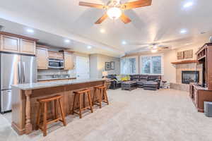 Kitchen featuring appliances with stainless steel finishes, tasteful backsplash, a breakfast bar, light colored carpet, and a tiled fireplace