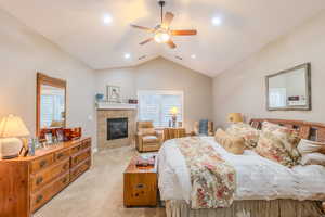 Carpeted bedroom featuring a tile fireplace, ceiling fan, and vaulted ceiling