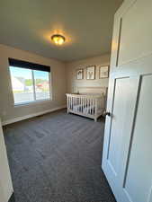 Unfurnished bedroom featuring a crib and dark colored carpet