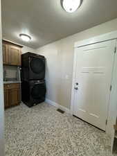 Laundry room with cabinets, stacked washer and dryer, and sink