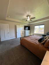 Carpeted bedroom with a tray ceiling, ensuite bath, ceiling fan, and a textured ceiling