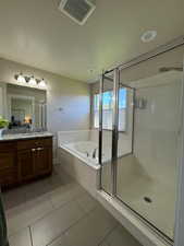 Bathroom featuring tile patterned flooring, shower with separate bathtub, and vanity