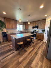 Kitchen featuring appliances with stainless steel finishes, light stone counters, pendant lighting, a center island, and a breakfast bar area