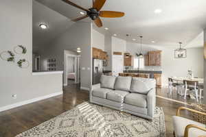 Living room featuring ceiling fan with notable chandelier, high vaulted ceiling, dark wood-type flooring, and sink