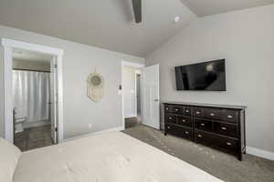 Carpeted bedroom with ensuite bathroom, ceiling fan, and vaulted ceiling