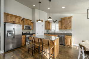 Kitchen with high vaulted ceiling, a kitchen island, decorative backsplash, and appliances with stainless steel finishes