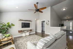 Living room with dark hardwood / wood-style flooring, vaulted ceiling, and ceiling fan