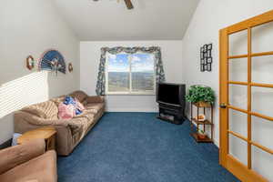 Living room with ceiling fan, dark carpet, and lofted ceiling