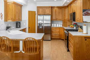 Kitchen featuring sink, stainless steel appliances, kitchen peninsula, light hardwood / wood-style floors, and a breakfast bar