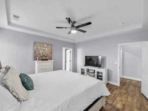 Bedroom with ceiling fan, dark hardwood / wood-style flooring, and a raised ceiling