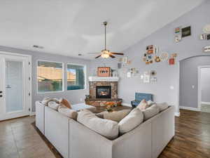 Living room featuring a fireplace, dark hardwood / wood-style floors, vaulted ceiling, and ceiling fan