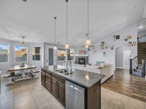 Kitchen featuring stainless steel dishwasher, dark brown cabinetry, sink, a stone fireplace, and an island with sink