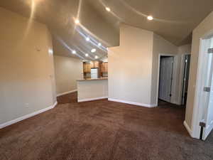 Unfurnished living room with dark colored carpet and lofted ceiling