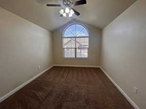 Carpeted spare room featuring ceiling fan and vaulted ceiling