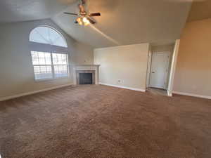 Unfurnished living room featuring ceiling fan, lofted ceiling, carpet floors, and a tiled fireplace