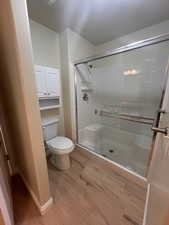 Bathroom featuring wood-type flooring, toilet, and an enclosed shower