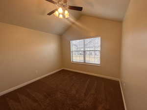 Unfurnished room with ceiling fan, dark carpet, and vaulted ceiling