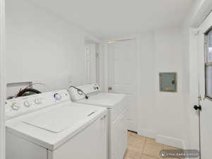 Washroom featuring washer and clothes dryer, light tile patterned floors, and electric panel