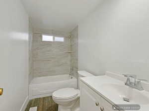 Full bathroom featuring vanity, wood-type flooring, tiled shower / bath combo, and toilet