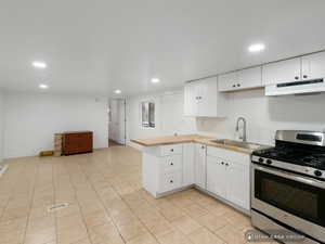 Kitchen with white cabinetry, sink, stainless steel range with gas cooktop, kitchen peninsula, and light tile patterned floors