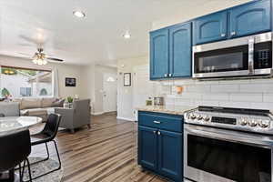 Kitchen with light stone countertops, backsplash, stainless steel appliances, and blue cabinets