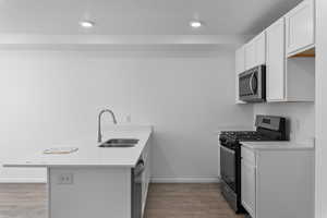 Kitchen with white cabinetry, sink, stainless steel appliances, kitchen peninsula, and laminate flooring