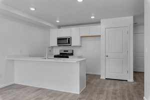 Kitchen with peninsula, sink, laminate flooring, gas stove, and white cabinetry