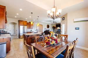 Dining area featuring ceiling fan with notable chandelier, light tile patterned floors, sink, and a tray ceiling