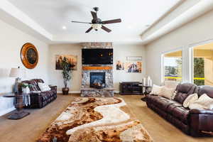 Carpeted living room with ceiling fan, a raised ceiling, and a fireplace