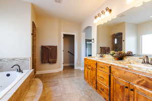 Bathroom featuring tile patterned flooring, a relaxing tiled tub, and vanity