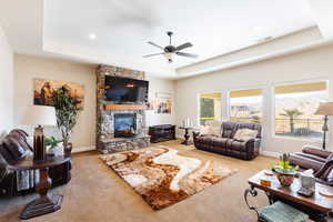 Carpeted living room featuring a tray ceiling, ceiling fan, and a fireplace